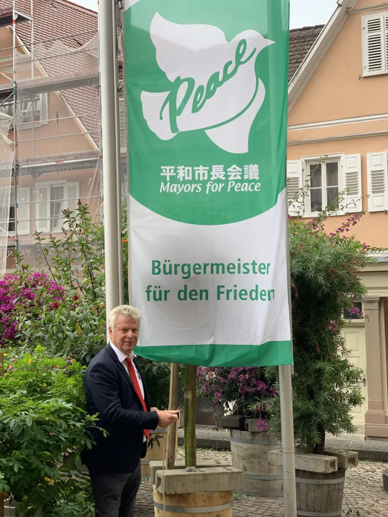 Ein Mann im Anzug hisst die wei&szlig;-gr&uuml;ne Mayors-for-Peace-Flagge in Bietigheim-Bissingen (Baden-W&uuml;rttemberg)